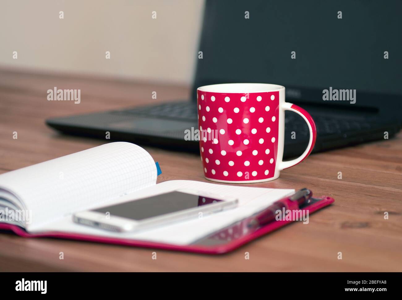 Arbeiten zu Hause - Computer und Notebook mit Teetaßteil. Tasse Cappuccino und Notebook in der Nähe von Telefon und Laptop auf Holztisch. Stockfoto