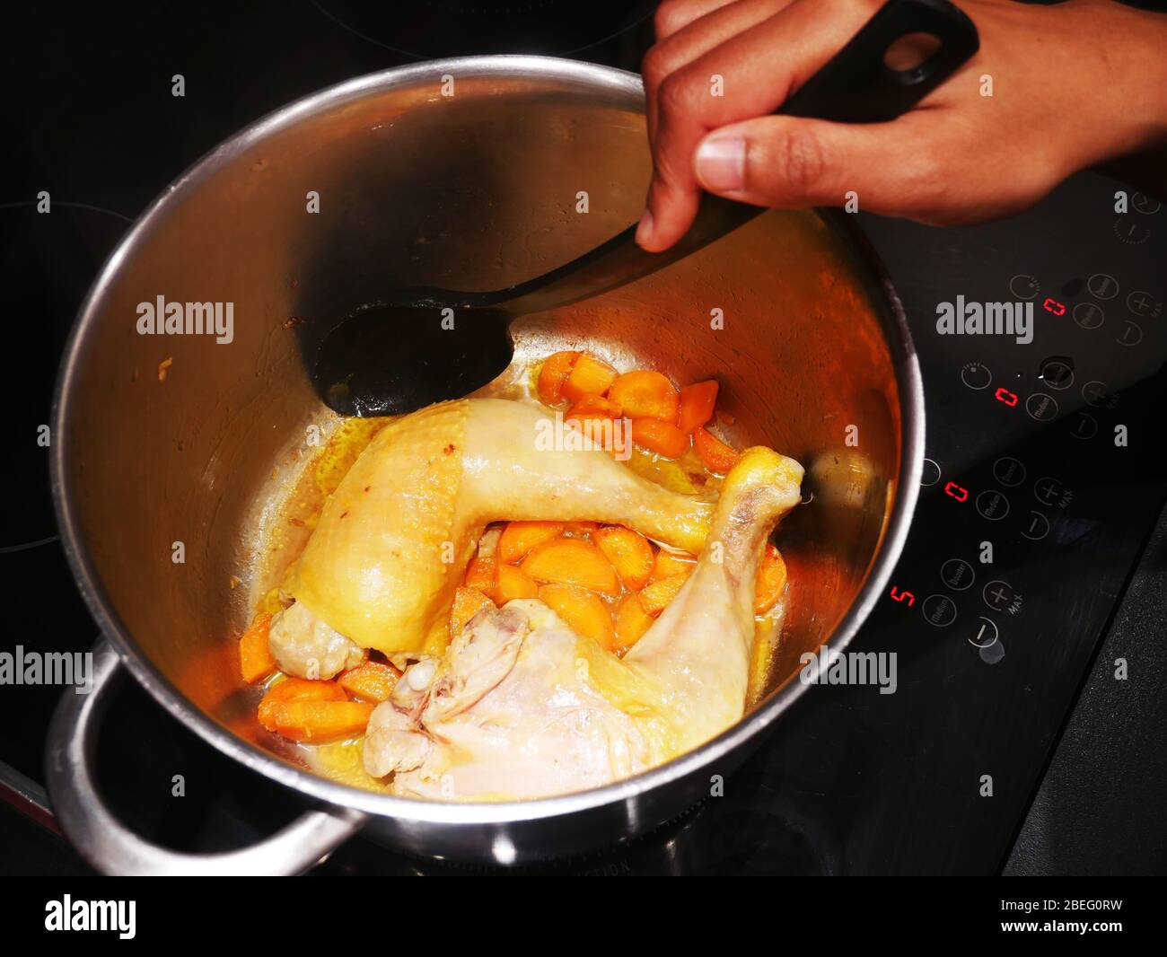Eine Frau kocht Hühnerschenkel, Karotten und Zwiebeln in einem Topf Stockfoto