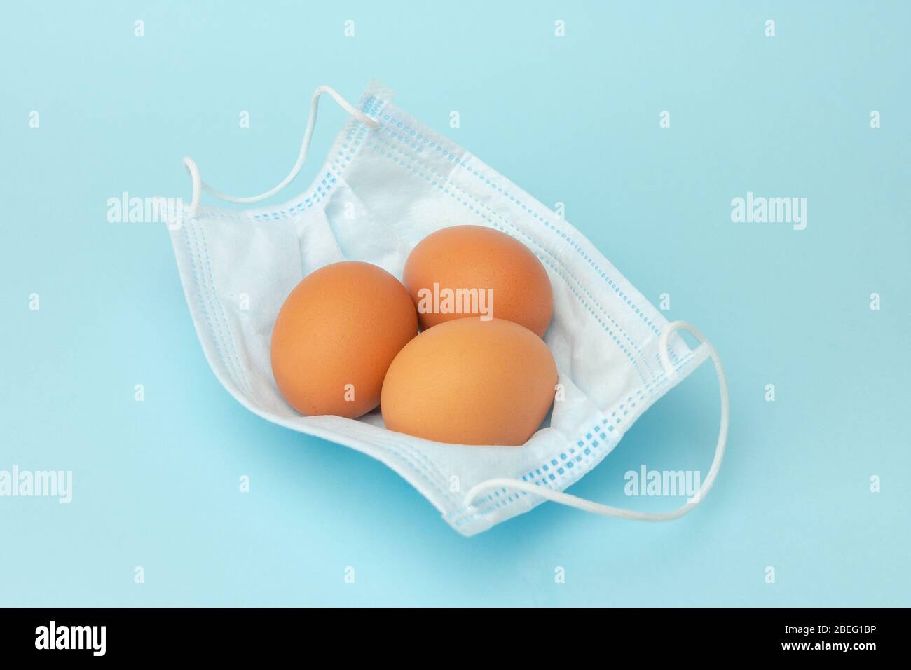 Ostern in der Zeit der Coronavirus-Pandemie. Eier sind in chirurgischer Schutzmaske auf blauem Hintergrund Stockfoto