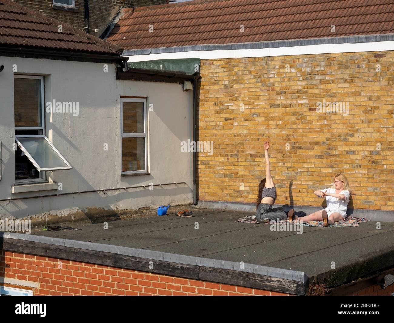 London. Leyton. GROSSBRITANNIEN. April 2020. Blick auf zwei junge Frauen beim Sonnenbaden und beim Training auf dem Dach während der Lockdown Covid-19. Stockfoto