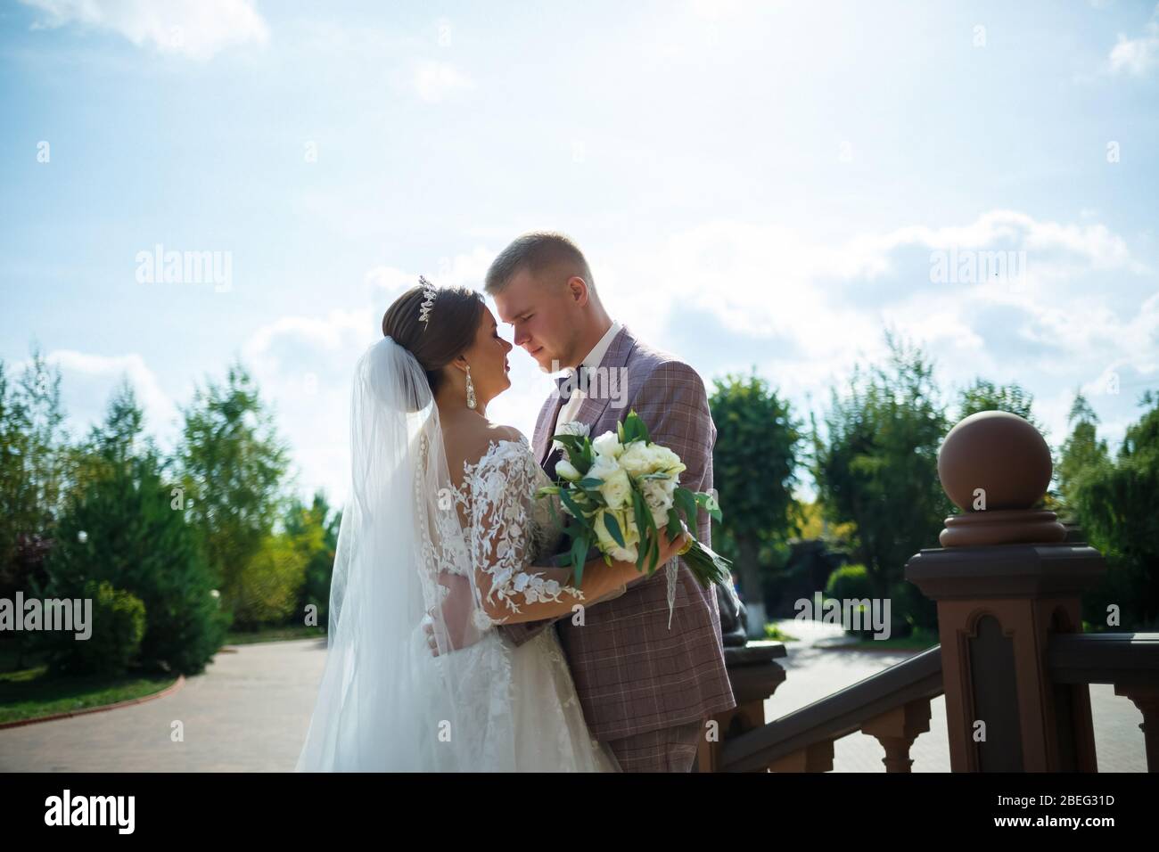 Braut im weißen Kleid und Bräutigam in Kostüm kuscheln und spazieren im Park Stockfoto