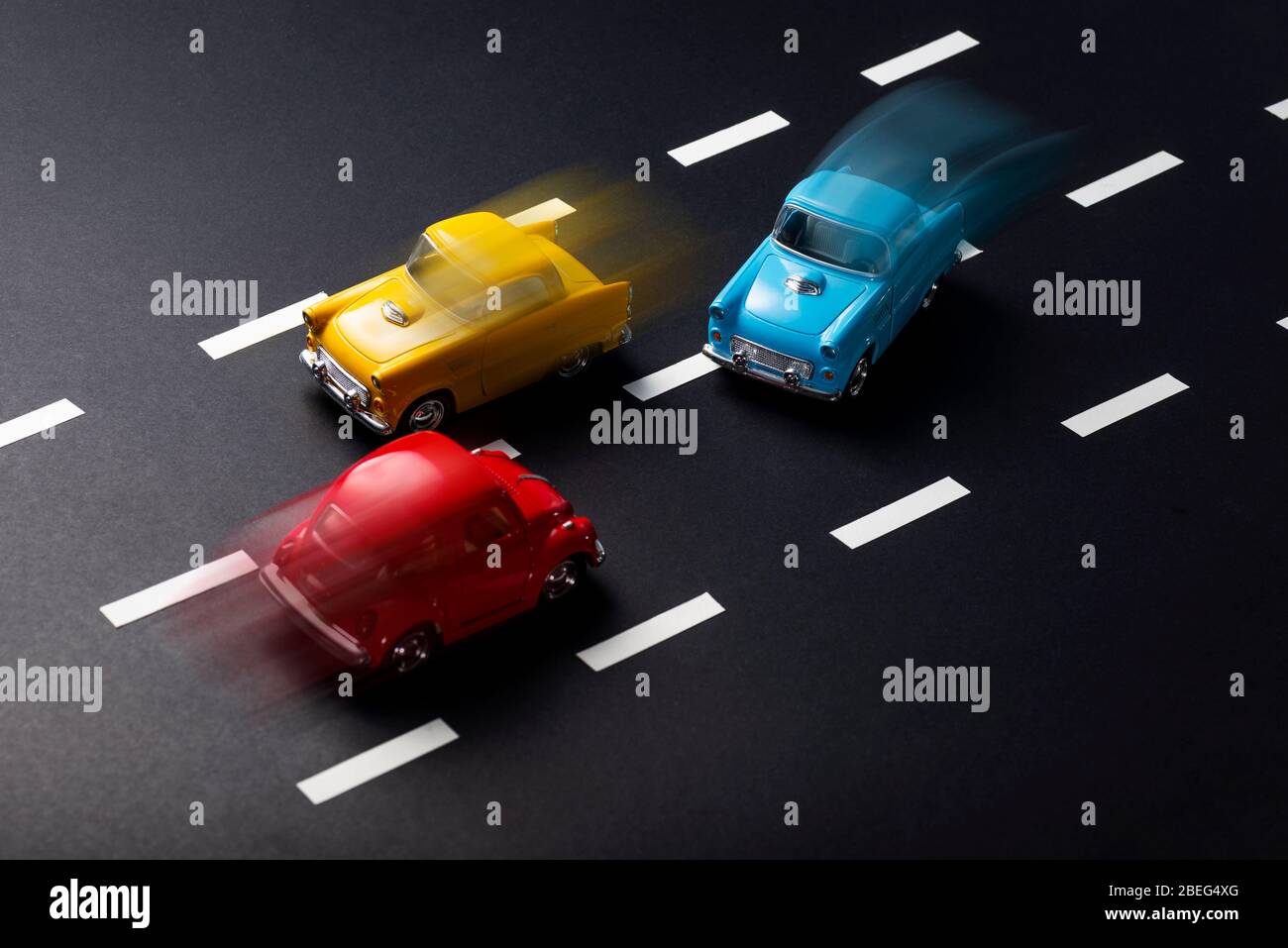 Falsche Überholmanschieren mit Bewegungsunschärfe durch Spielzeugmodellautos auf einer Straße mit Streifen. Stockfoto
