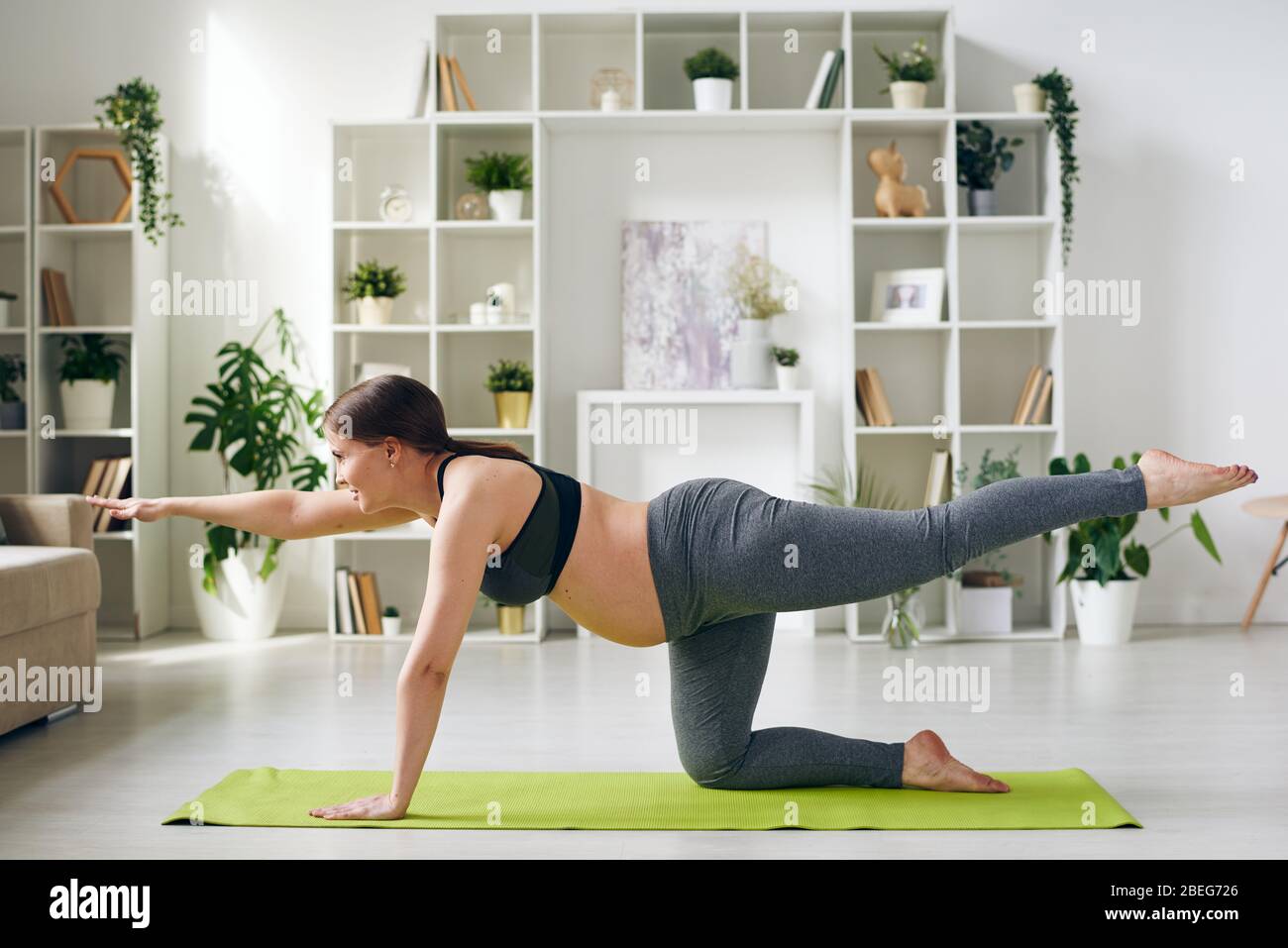 Energetische junge schwangere Frau in Sportbekleidung üben Balancing Tisch Pose auf Yoga-Matte im Wohnzimmer Stockfoto
