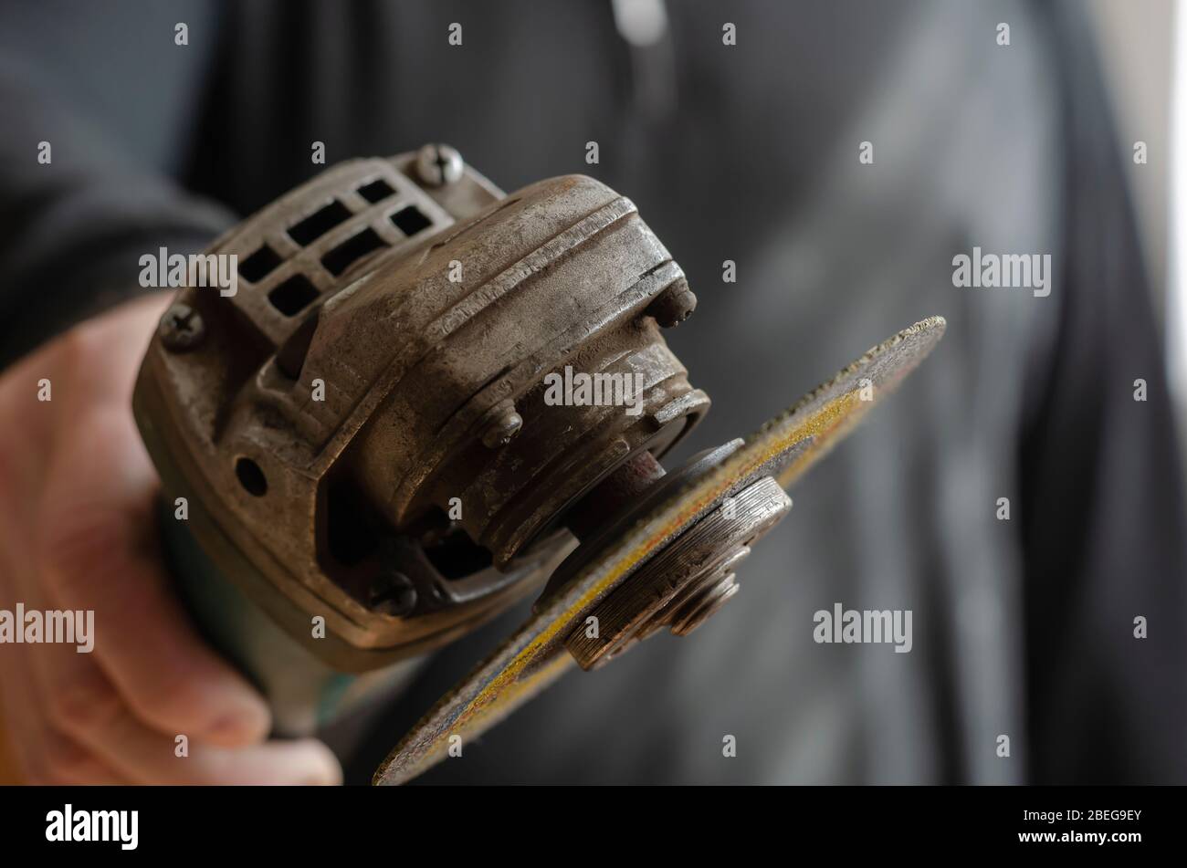 Ein Mann hält einen Winkelschleifer in die Kamera. Ein kleines Elektrowerkzeug in der Hand. Arbeitssicherheit in der Produktion. Selektiver Fokus. Unscharfer Hintergrund. Stockfoto