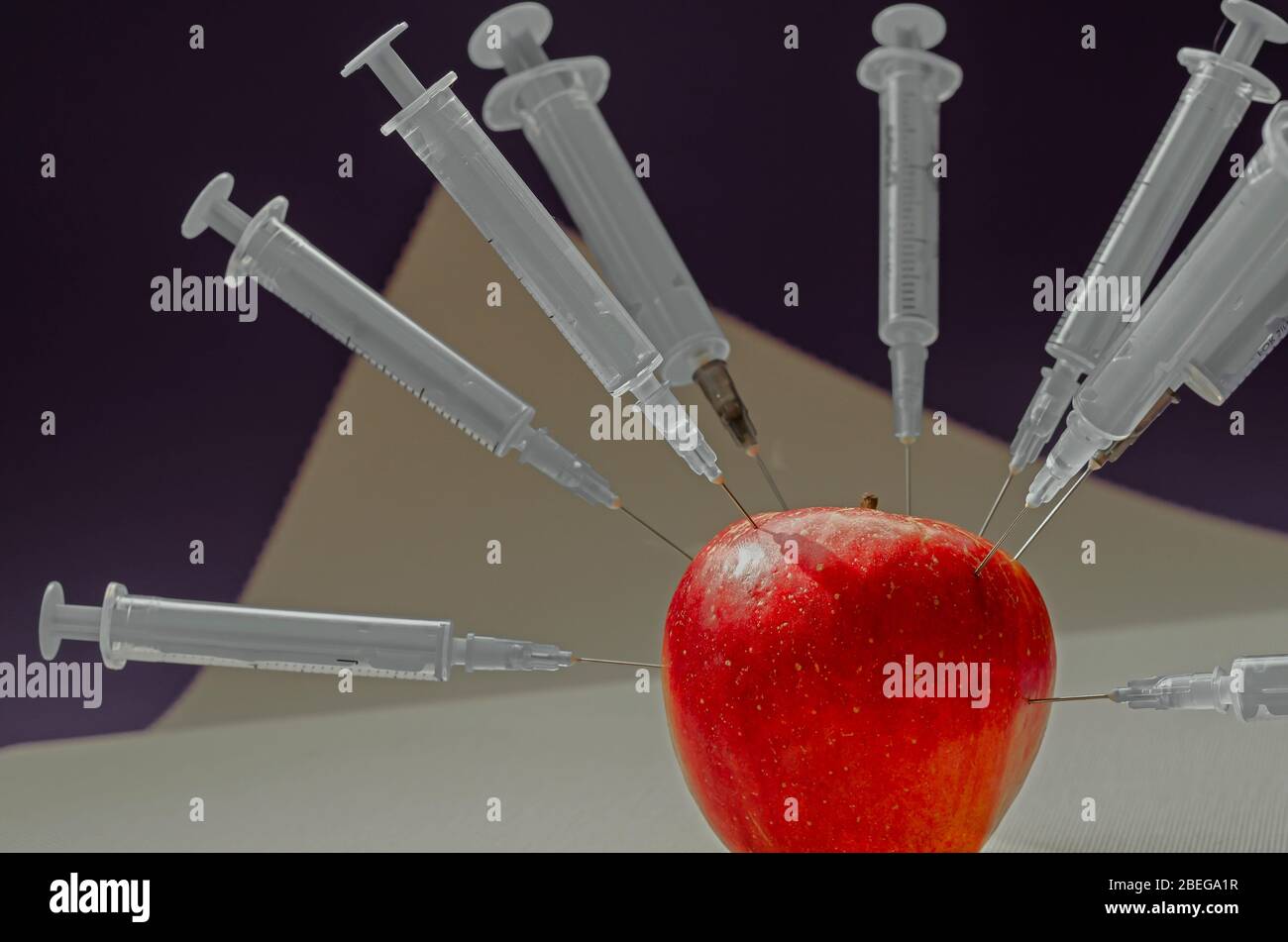 Apfel mit Spritzen besetzt. Reifer roter apfel von allen Seiten von Spritzen durchbohrt. Gesundheitswesen oder Kosmetologie. Mehrdeutiger Hintergrund. Seitenansicht. Selektiv Stockfoto