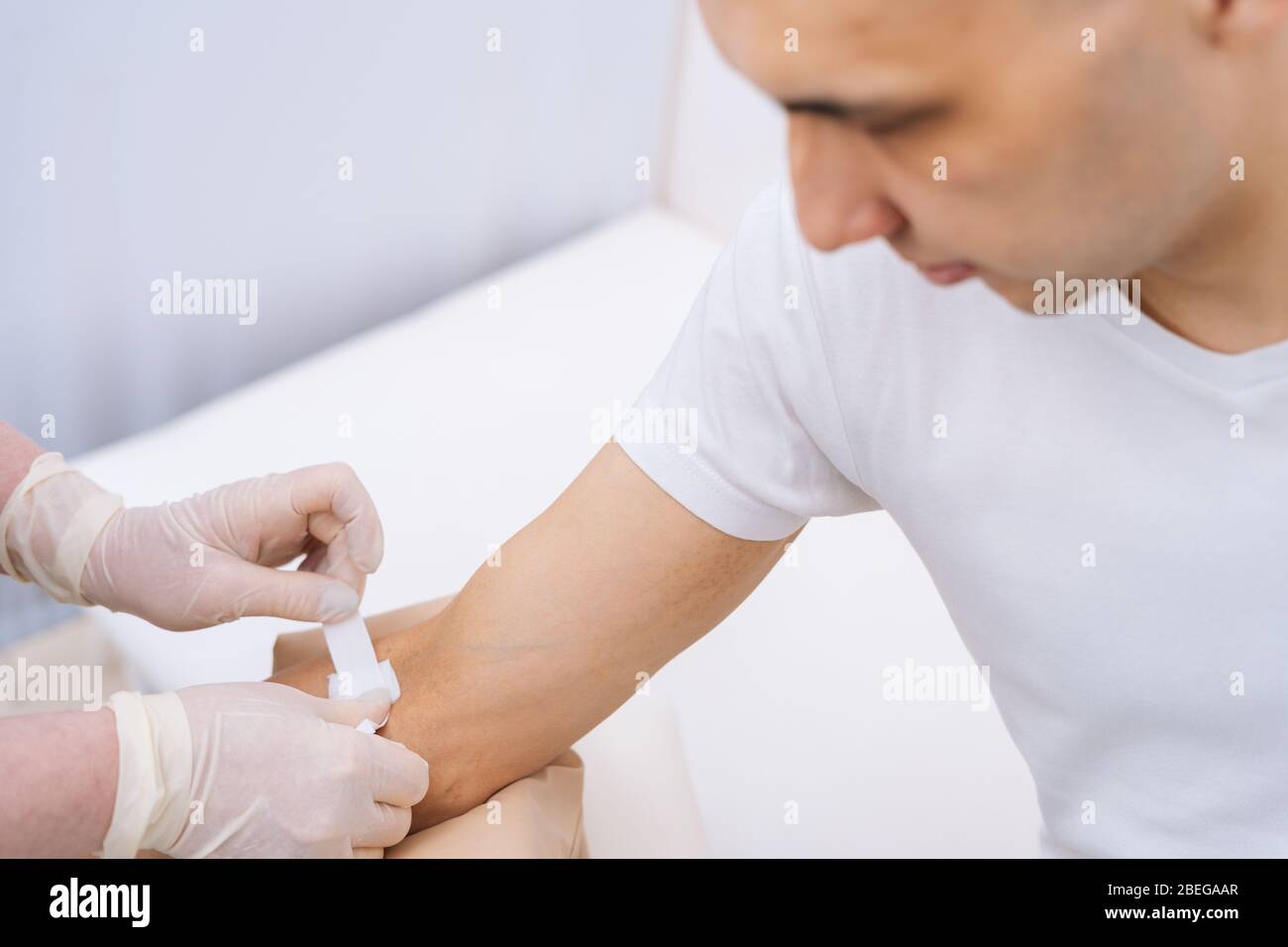 Krankenschwester in Gummischutzhandschuhen, die einen Klebeverband auf den Arm des jungen Mannes legt Stockfoto