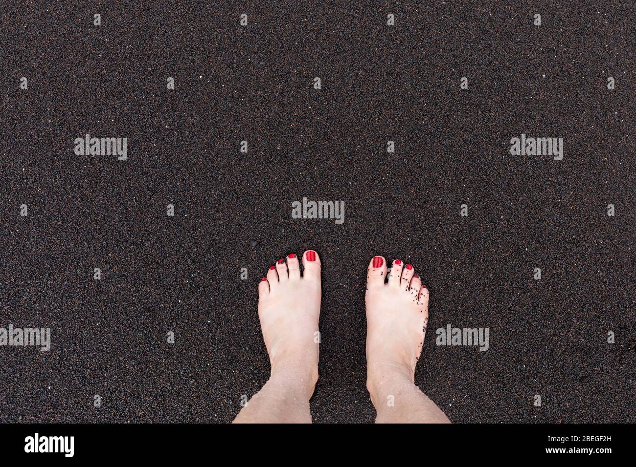 Die Füße einer Frau am schwarzen Sandstrand in Hana, Maui, Hawaii Stockfoto