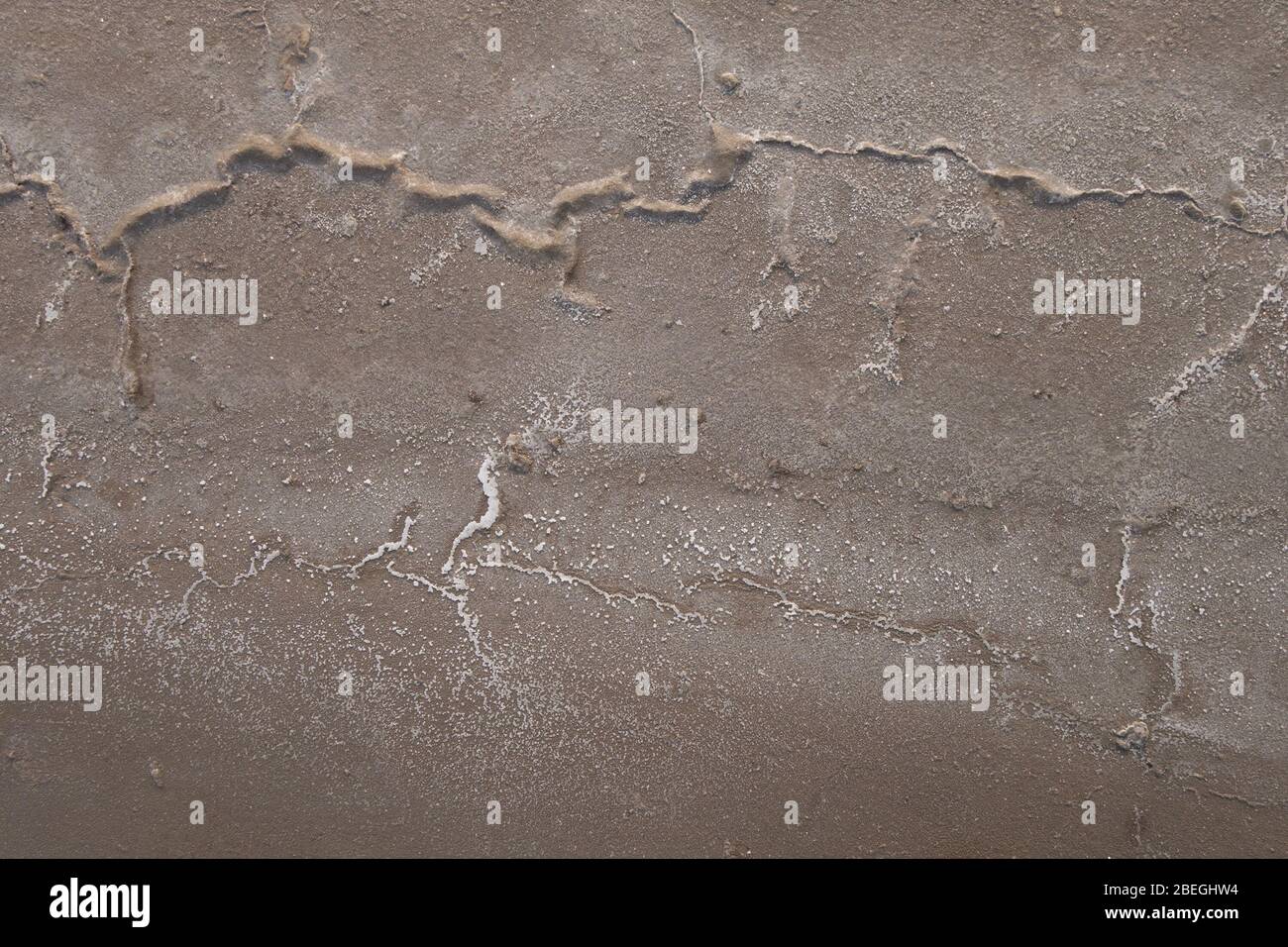 Sandiger Boden des getrockneten Reservoirs mit den Rissen und den Salzkristallen. Stockfoto