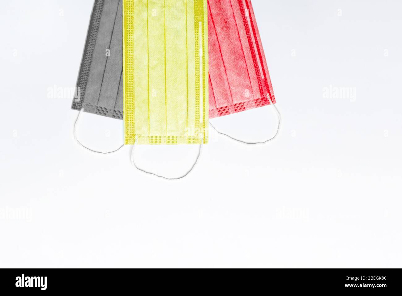 Auf der Oberseite sind 3 medizinische Masken in den Farben schwarz, gelb und rot auf einem hellen Hintergrund. Masken sind in der Flagge von Belgien gesammelt. Medizin Konzept in belg Stockfoto