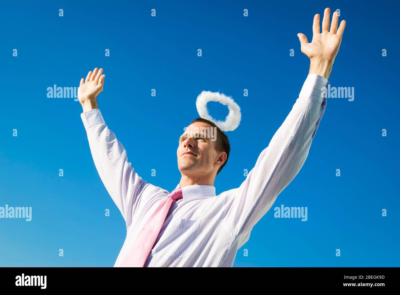 Engelhafte Geschäftsmann stehend Arme mit einem Heiligenschein schweben über seinem Kopf in den blauen Himmel angehoben Stockfoto