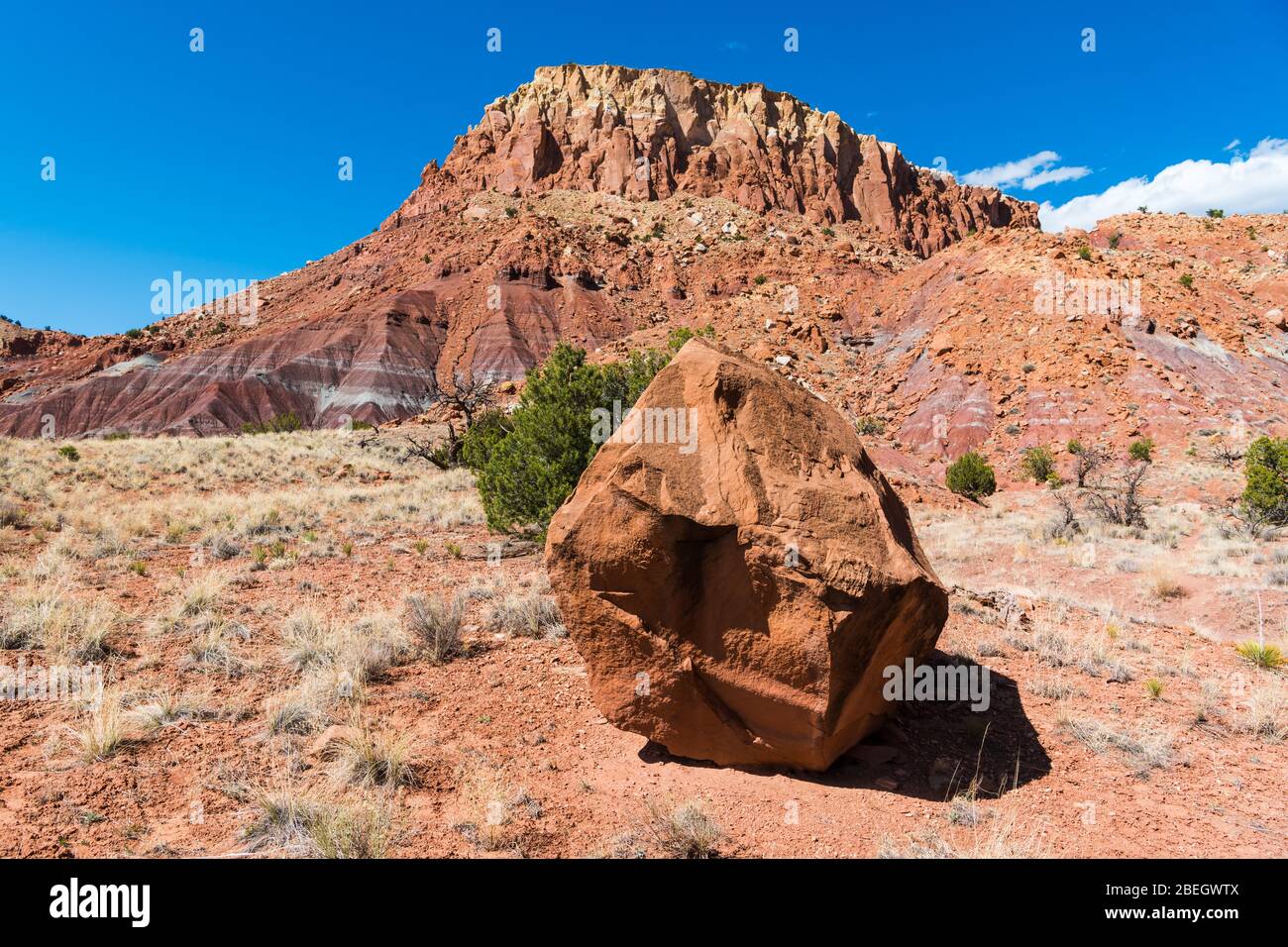 Großer Felsblock in einer Wüstenlandschaft mit einem bunten mesa im Hintergrund bei Abiquiu, New Mexico Stockfoto