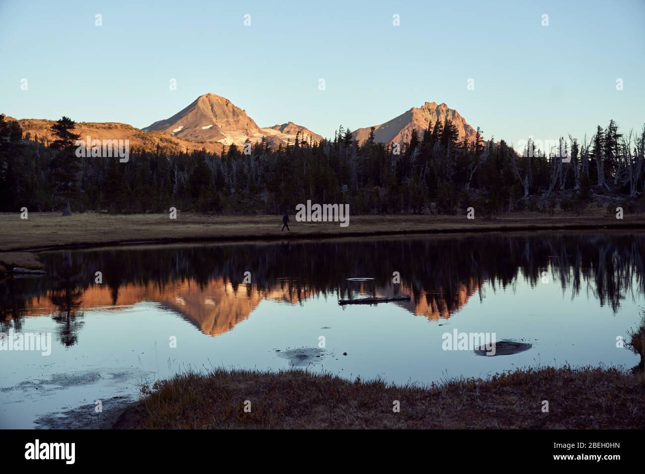 Person, die am See entlang geht, mit Bergen im Hintergrund Stockfoto
