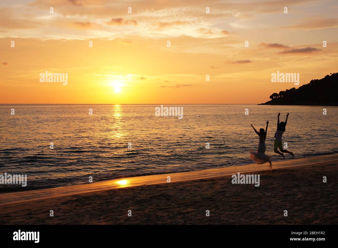 Wunderschöne Küste mit Sonnenlicht durchdringt den Himmel. Ein Paar, das vor dem Sonnenuntergang hüpfte, genossen die exotische und berauschende Stimmung Stockfoto
