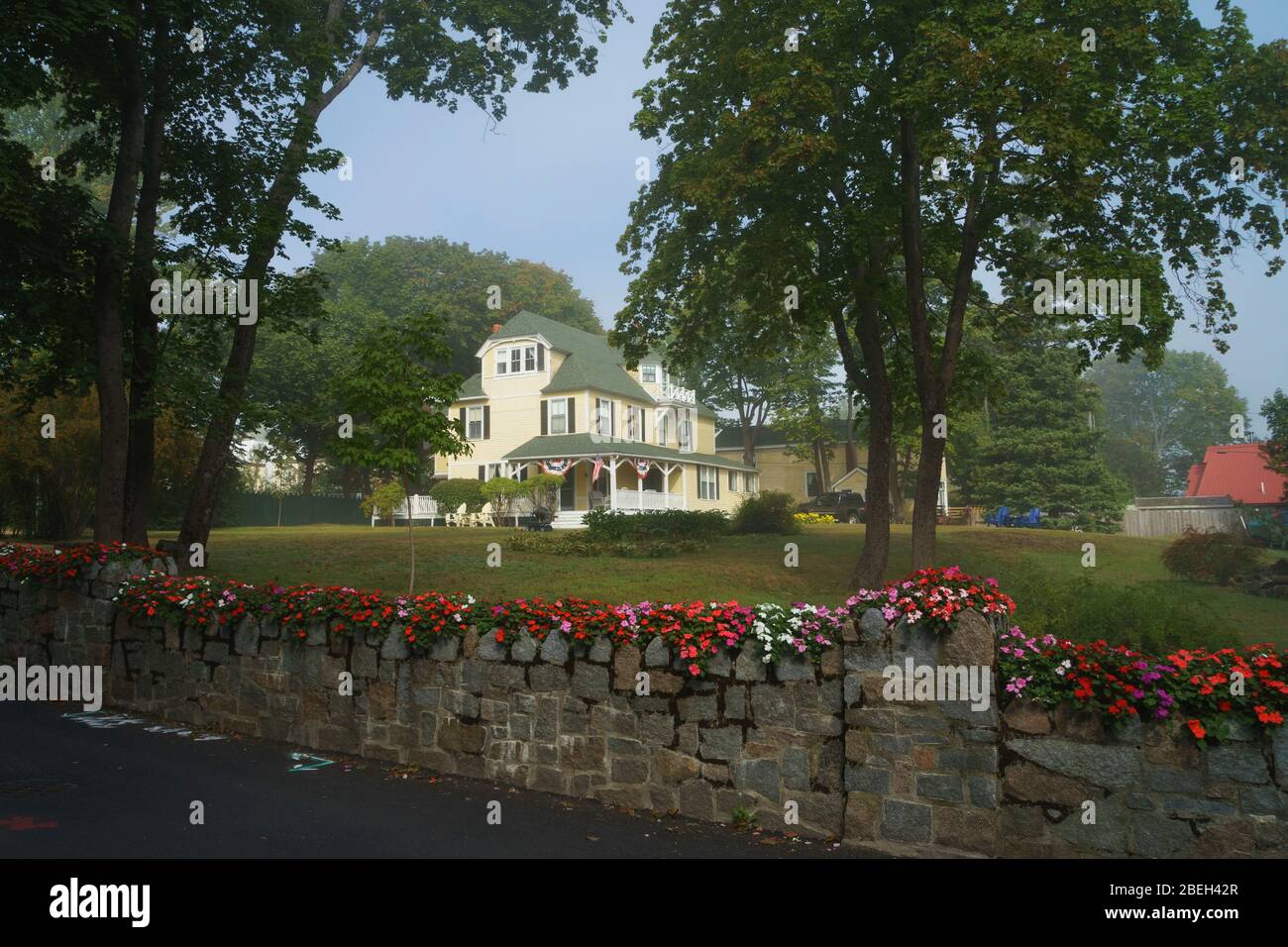 Malerisches dreistöckiges Haus mit einem weitläufigen Rasen, der von einer Steinmauer mit Blumen umgeben ist. Bar Harbor, Maine, USA. Stockfoto