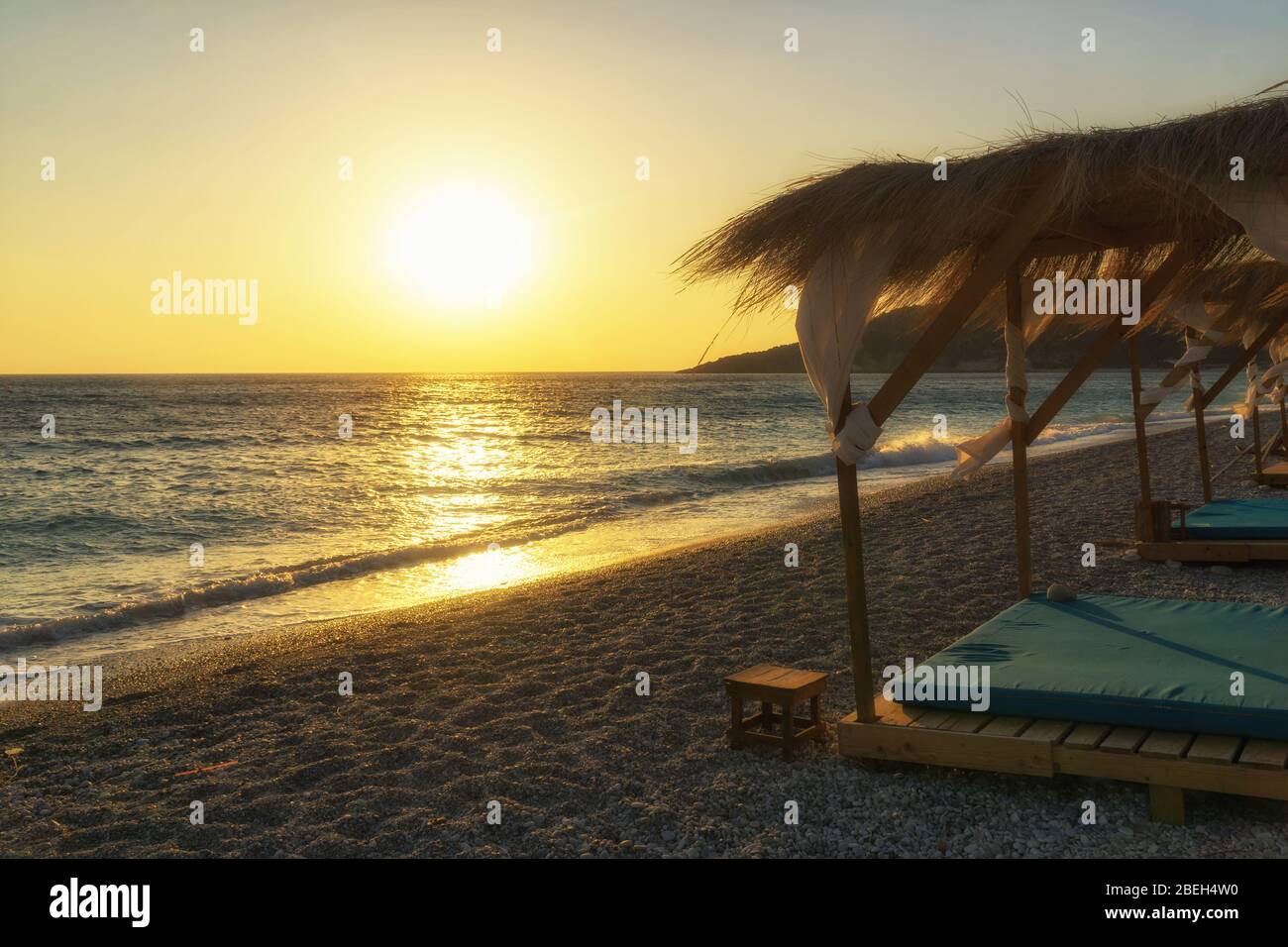 Sonnenuntergang am Strand Livadi bei Himare, Albanien, Europa. Strandhaus mit Sonnenliegen am Strand Ionische Küste. Stockfoto
