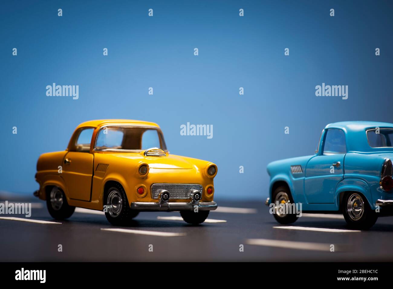 Zwei Spielzeug cas ein blau und ein gelb auf einem blauen Hintergrund und Asphaltstraße gefärbt. Stockfoto