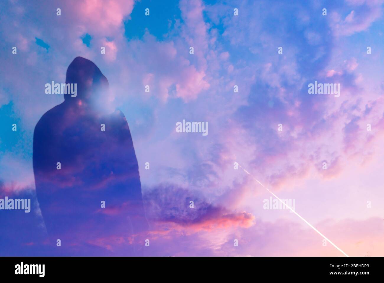 Eine doppelte Belichtung einer launischen, Kapuzenfigur, die gegen den Sonnenuntergang schlingt. Mit gezielter Streulicht. Mit einem abstrakten, experimentellen Traum wie edi Stockfoto