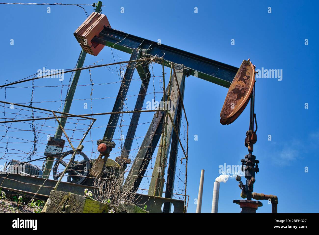 Pumpjack Oil Well mit Rauchstapeln im Hintergrund. Stockfoto