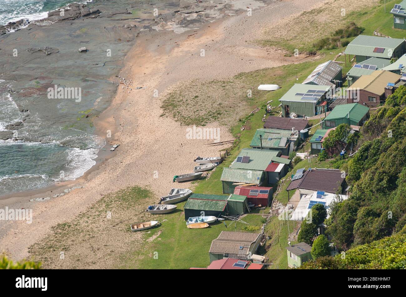 Luftaufnahme von Fischerhäusern mit Solarpaneelen und Junk-Booten an einem Strand an einem Ufer. Otford, Australien Stockfoto