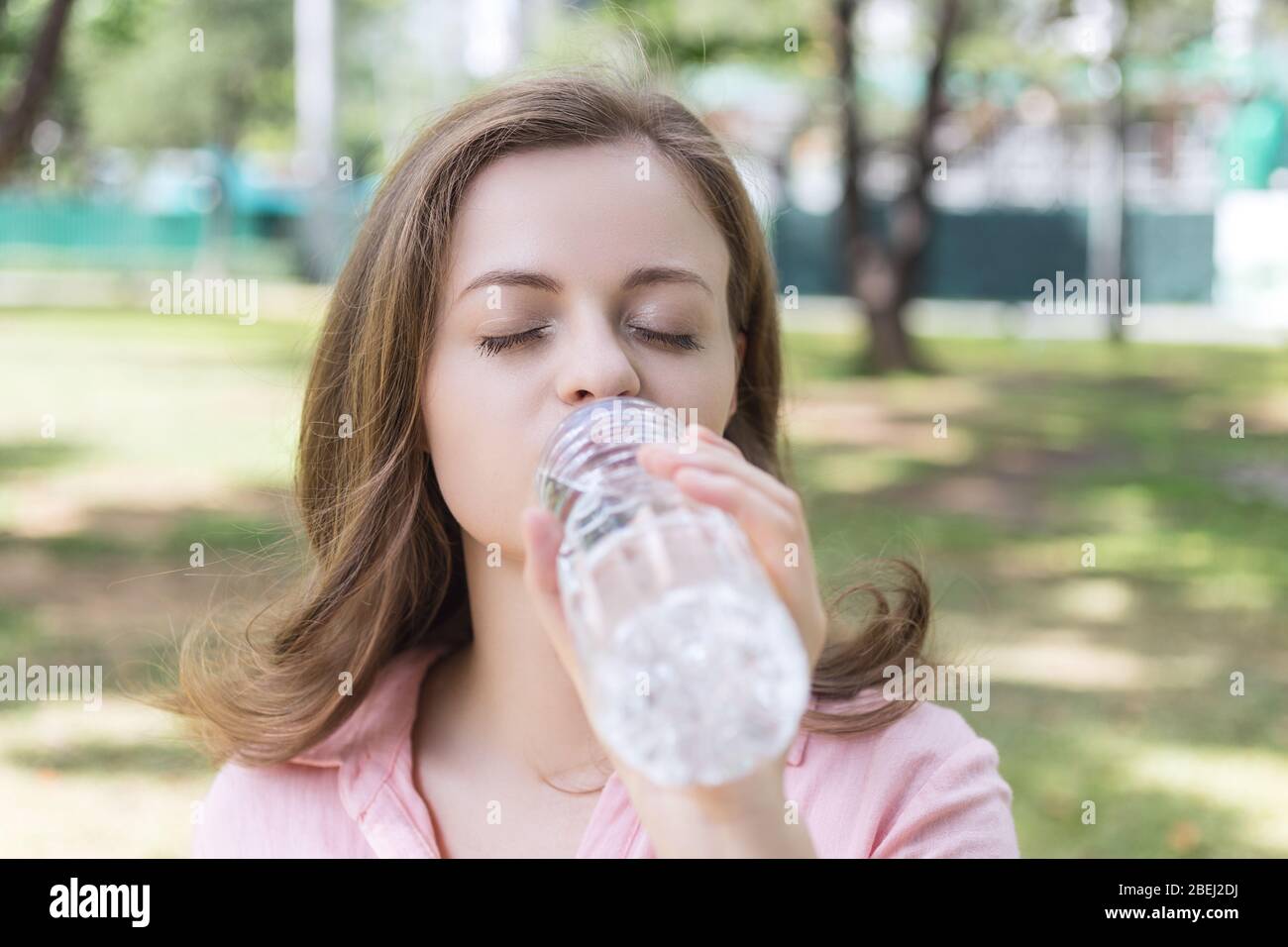 Junge kaukasische Frau Mädchen trinken Wasser aus einer Plastikflasche im grünen Park, Nahaufnahme Stockfoto