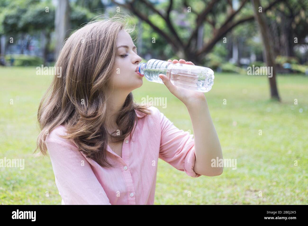 Junge kaukasische Frau Mädchen Trinkwasser aus einer Plastikflasche im grünen Park Stockfoto