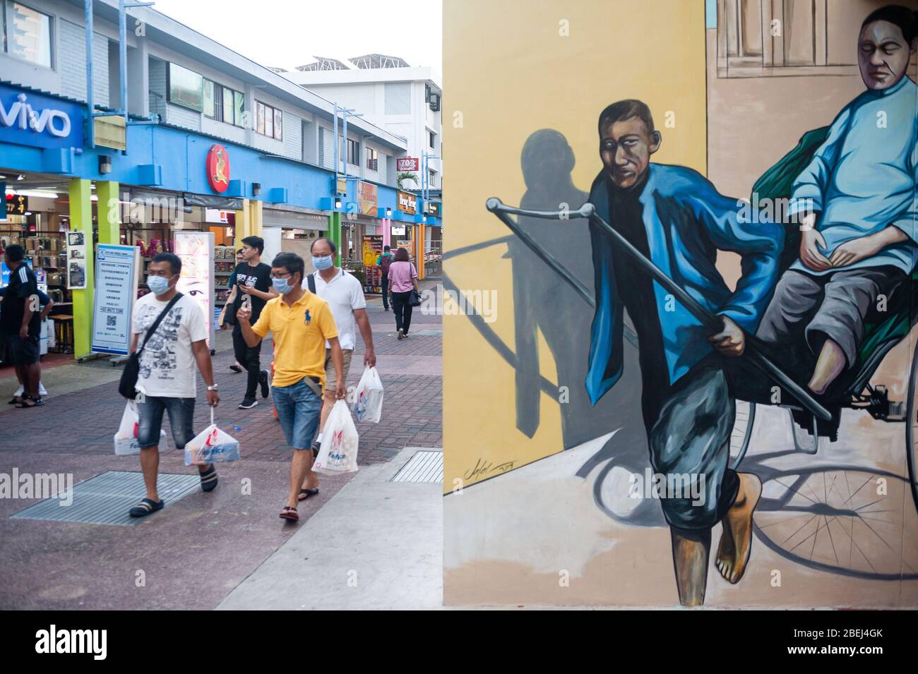 25.03.2020, Singapur, Republik Singapur, Asien - Männer mit Gesichtsmasken gehen an einer Wandmalerei vorbei, die eine traditionelle Rikscha in einer Fußgängerzone darstellt. Stockfoto