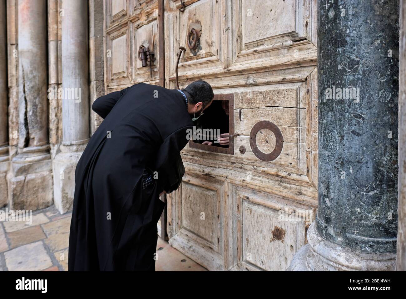 Ein Mitglied der koptischen Gemeinschaft trägt eine Schutzmaske, während er durch eine kleine Luke in der verschlossenen Haupttür der Grabeskirche zu einem der Mönche spricht, inmitten von Einschränkungen aufgrund der Coronavirus (COVID-19)-Pandemie in der Altstadt von Jerusalem Israel Stockfoto