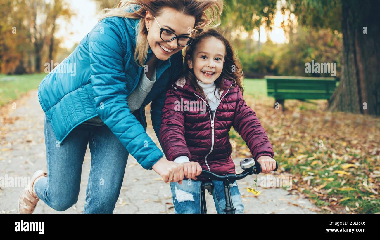 Schöne Mutter mit Brille versucht, ihre Tochter zu lehren, das Fahrrad in einem Park zu fahren Stockfoto