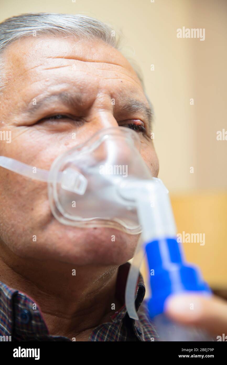 Leitender Mann, der medizinische Geräte für die Inhalation mit Atemschutzmaske verwendet, Vernebler im Zimmer Stockfoto