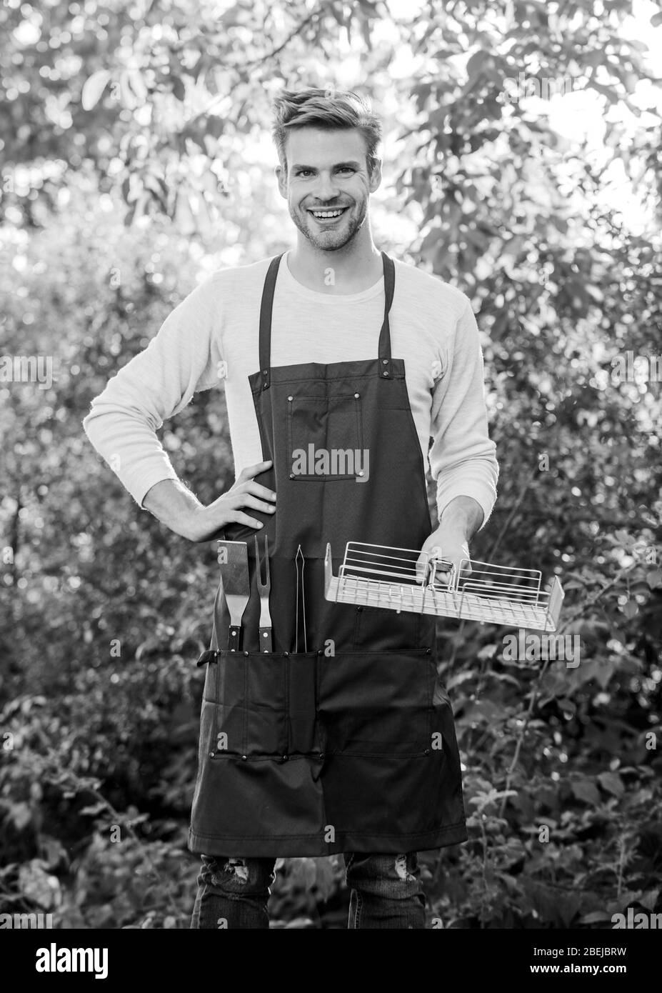 Genießen Sie glückliche Momente. Familienwochenende Ausflug. Sommerpicknick. Mann Grillgrill. Werkzeuge zum Braten von Fleisch im Freien. Picknickgeschirr. Party-Wochenende im Freien. Kulinarisch. Koch kocht grillkost. Stockfoto