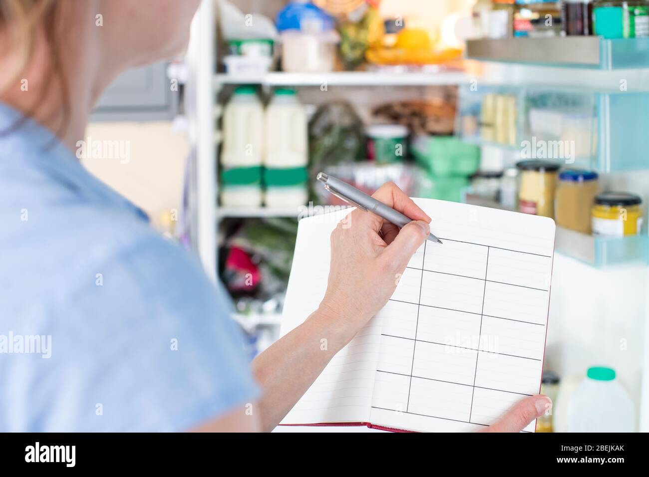 Frau Steht Vor Dem Kühlschrank In Der Küche Mit Notizbuch Schreiben Wöchentliche Mahlzeit Plan Stockfoto