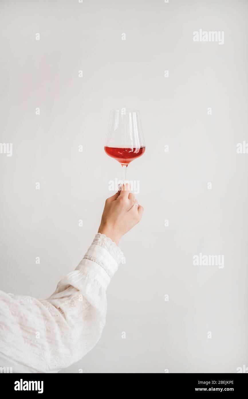 Frauen Hand hält Glas Roséwein über weiße Wand Stockfoto