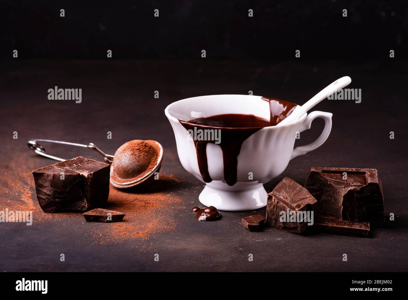 Auf einer dunklen rustikalen Oberfläche, eine Tasse heiße Schokolade, ein paar Stücke dunkle Schokolade und Kakaopulver Stockfoto