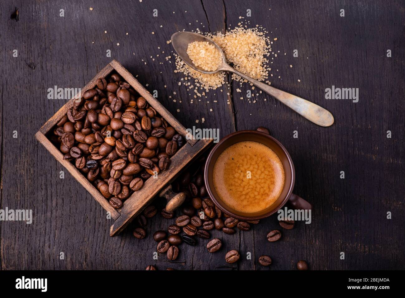 Auf dem rohen und dunklen Holztisch eine Tasse Kaffee mit einem Löffel braunem Zucker und gerösteten Kaffeebohnen. Stockfoto