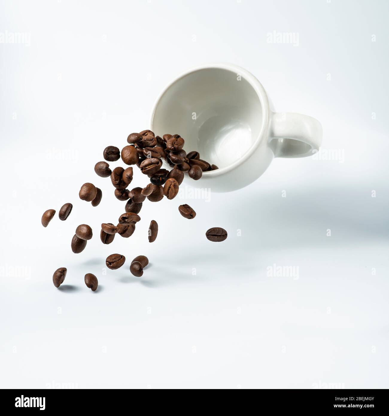 Isoliert vom weißen Hintergrund, eine Tasse Kaffee in der Luft, aus der eine Kaskade von gerösteten Kaffeebohnen fließt schweben Stockfoto