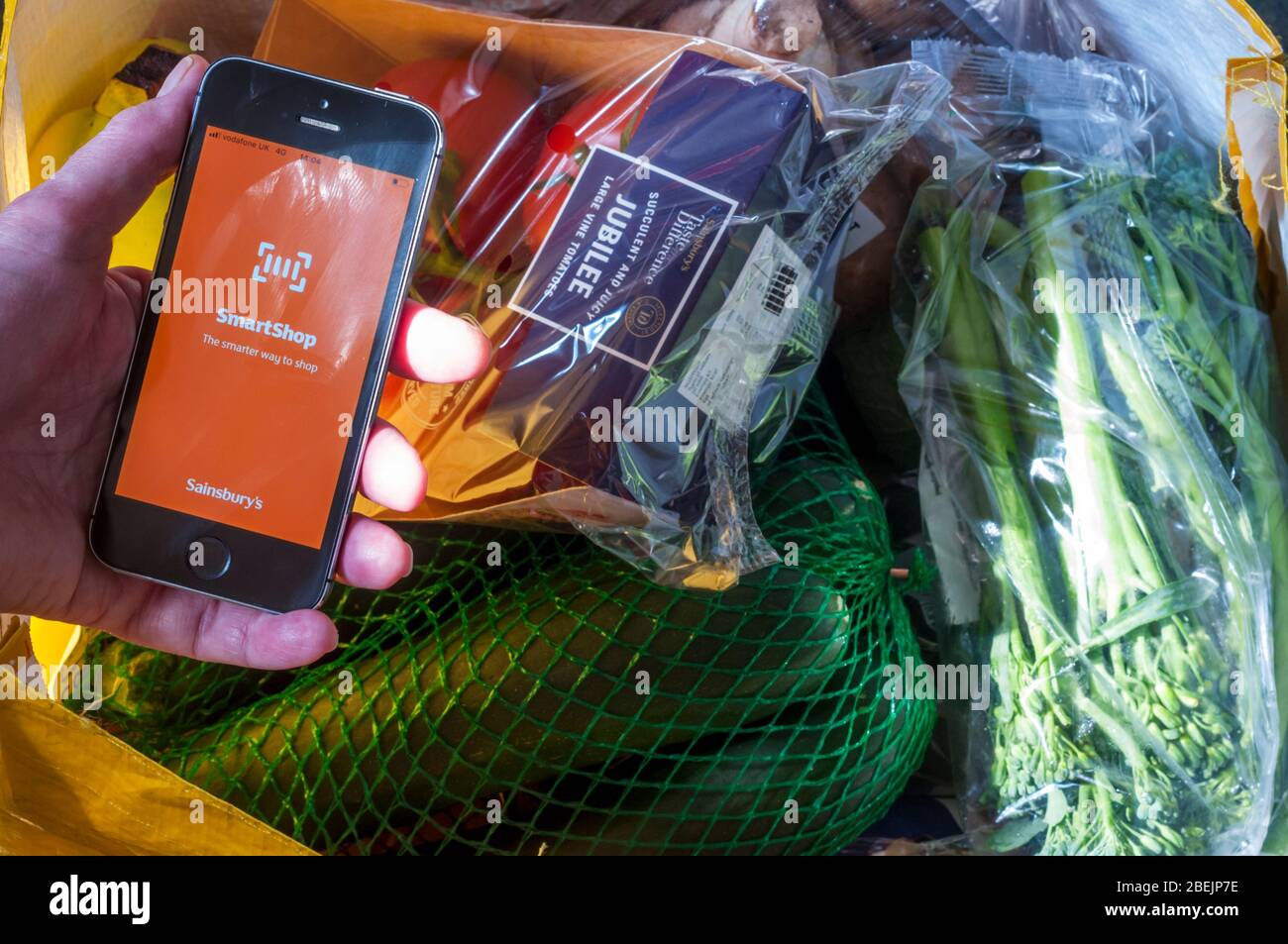Sainsbury's Smartshop elektronische Shopping App auf einem iPhone vor einer Tasche voller Einkäufe aus einem Sainsbury's Supermarkt. Stockfoto