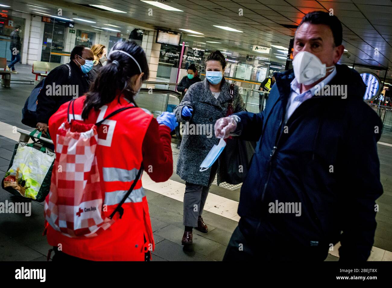 Barcelona, Katalonien, Spanien. 14. Apr 2020 - EIN Freiwilliger des Roten Kreuzes verteilt Schutzmaske unter Pendlern am Bahnhof Catalunya in Barcelona. Tausende von Menschen kehren zur Arbeit zurück, nachdem die spanische Regierung die strengsten Maßnahmen der Coronavirus-Haft aufzuheben hat. Quelle: Jordi Boixareu/Alamy Live News Stockfoto