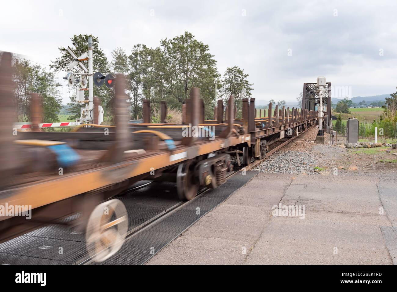 Eine Linie von Flachwagen, die von Diesellokomotiven an einem Bahnübergang durch die ländliche Stadt Paterson, New South Wales, Australien, abgeschleppt werden Stockfoto