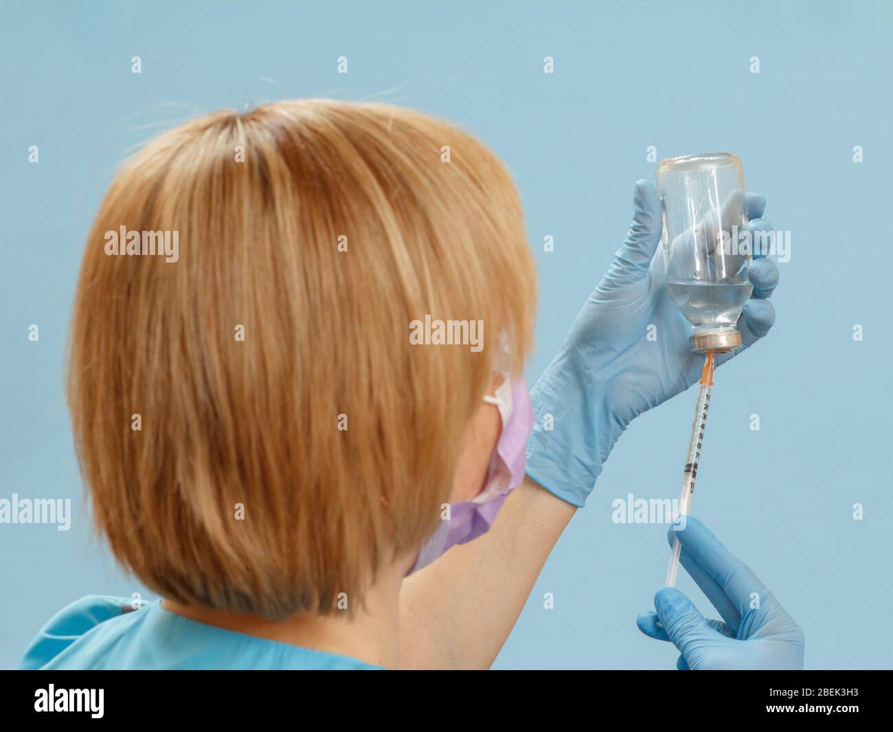 Ärztin, die eine Glasflasche hält und eine Spritze mit flüssigem Medikament zur Injektion auf blauem Hintergrund einfüllt. Selektiver Fokus auf Hände. Stockfoto