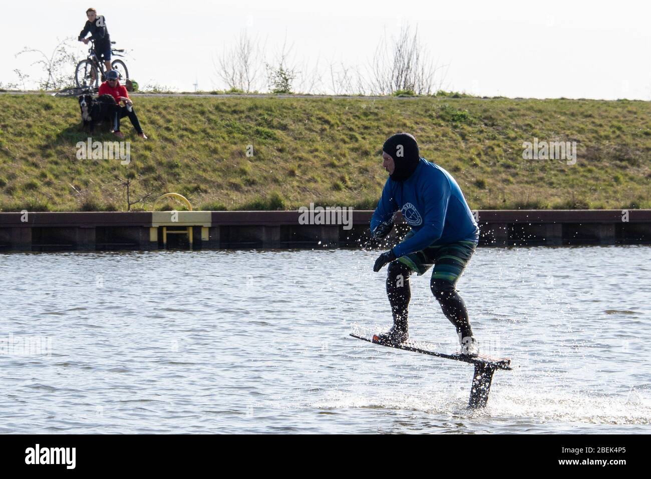 Wolmirstedt, Deutschland. April 2020. Paul Greifzu (48) praktiziert Hydrofoil-Surfen im Mittelandkanal, einer Trendsportart, die unter anderem von Australien nach Deutschland übergelaufen ist. Er wird von Radfahrern beobachtet. Quelle: Stephan Schulz/dpa-Zentralbild/ZB/dpa/Alamy Live News Stockfoto