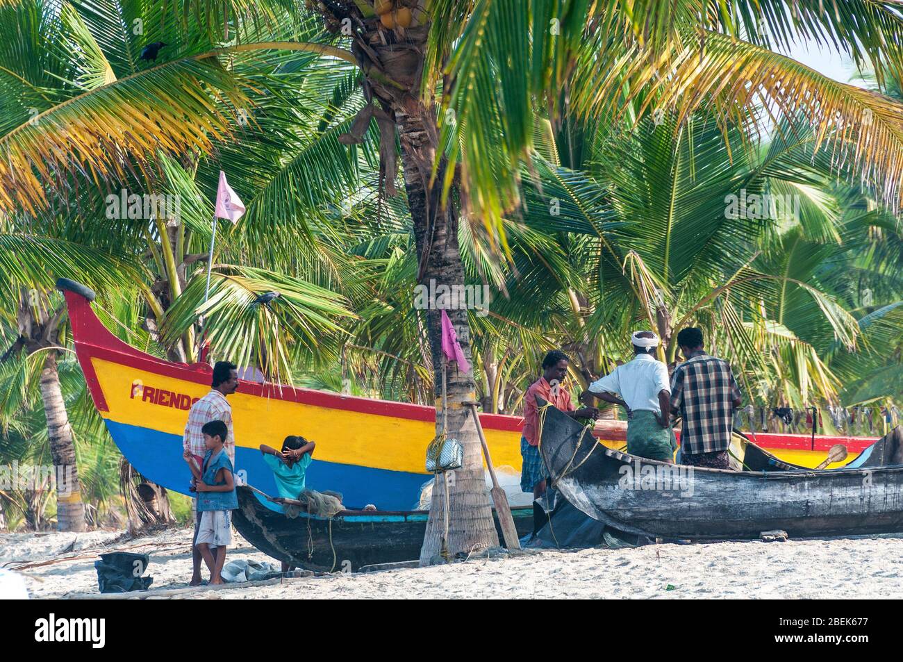 Familien entspannen neben ihren hölzernen Fischerbooten im kleinen Fischerdorf am Marari Beach, Mararikulam, Alapuzha District, Kerala, Indien Stockfoto