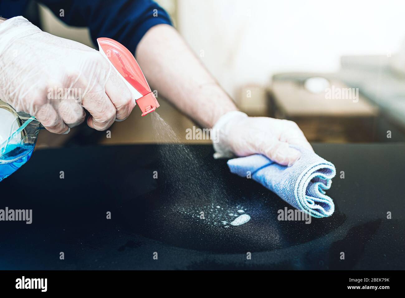 Nahaufnahme der Person, die Einweghandschuhe trägt und Desinfektionsmittel zur Reinigung der Tischoberfläche während der Coronavirus Covid-19-Pandemie verwendet Stockfoto