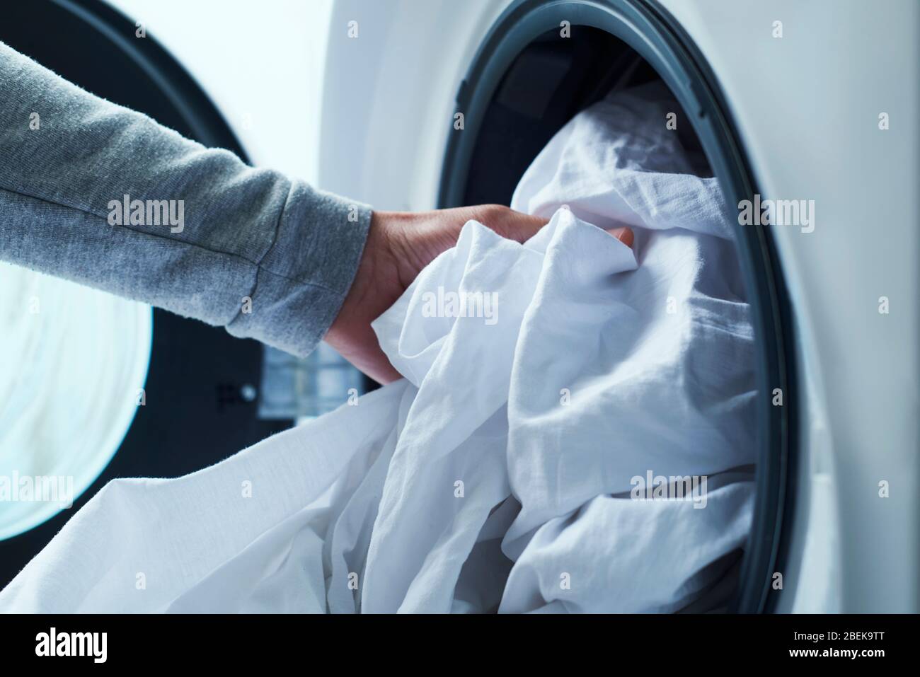 Nahaufnahme eines jungen kaukasischen Mannes, der weiße Bettwäsche in die Waschmaschine stellt Stockfoto