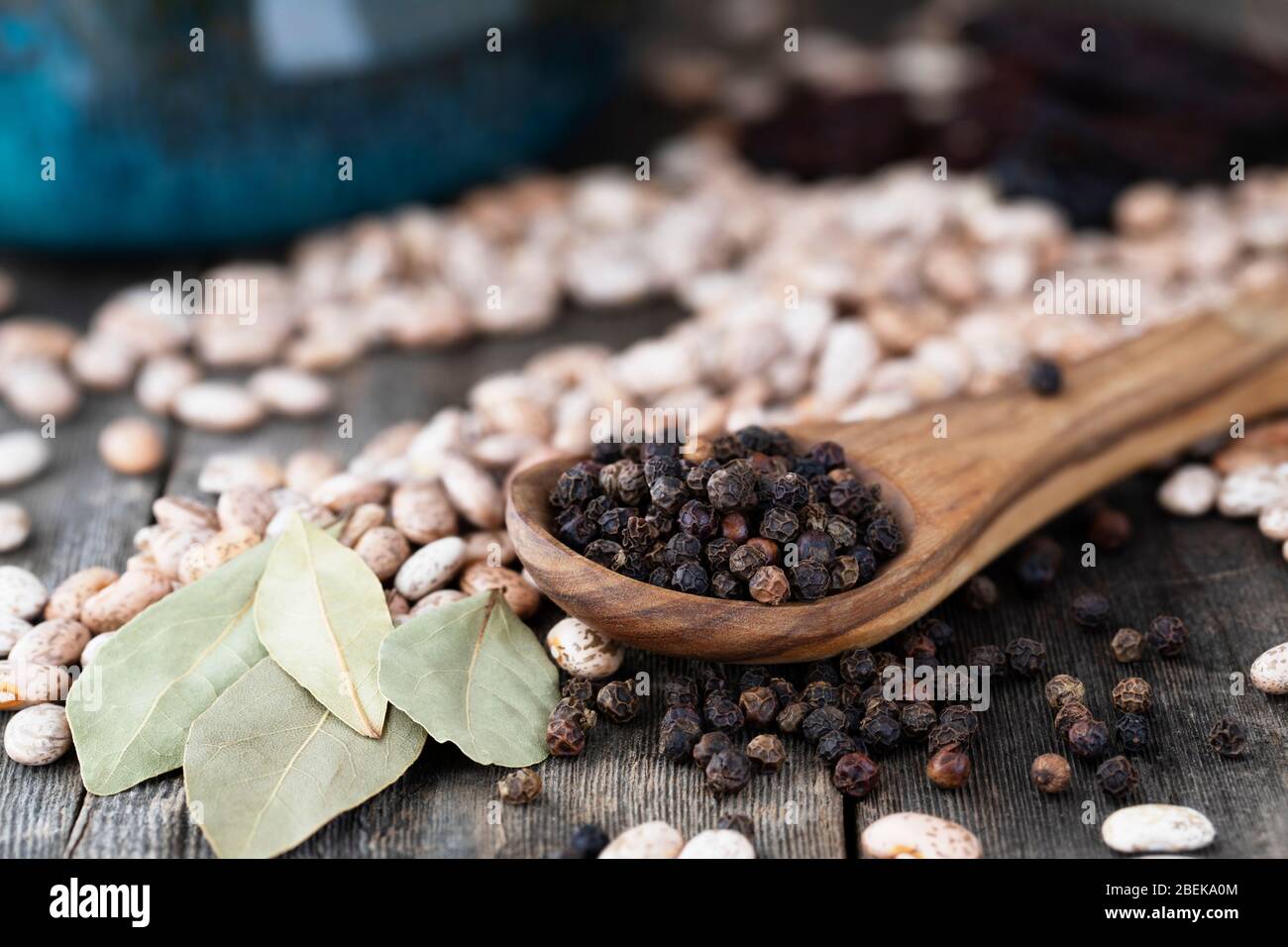 Holzlöffel voll schwarzer Pfefferkörner mit Pinto-Bohnen und Lorbeerblättern Stockfoto