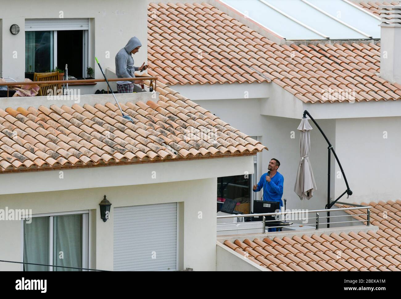 Altea La Vella, Provinz Alicante, Spanien, 21. März 2020, ein junger Mann auf seinem Balkon, der ein Handy benutzt, während sein Nachbar Musik auf seinem Computer macht Stockfoto