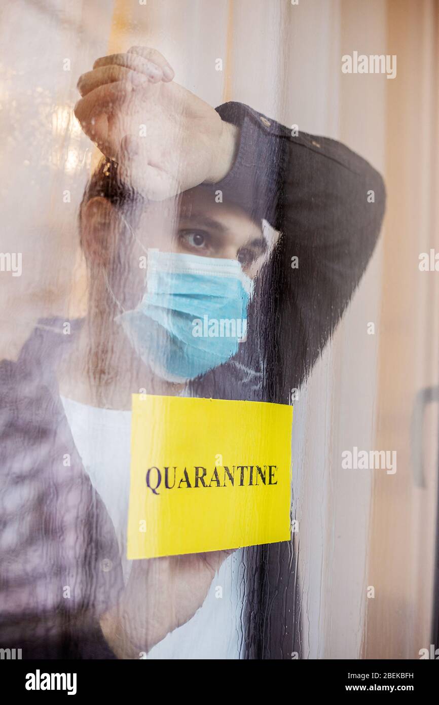 Einsamer Mann in Quarantäne mit Kovid 19 in Hausdämmung. Gelbes Warnzeichen mit Text Quarantäne im Fenster. Vorbeugung gegen eine Coronavirus-Pandemie. Mann in Stockfoto