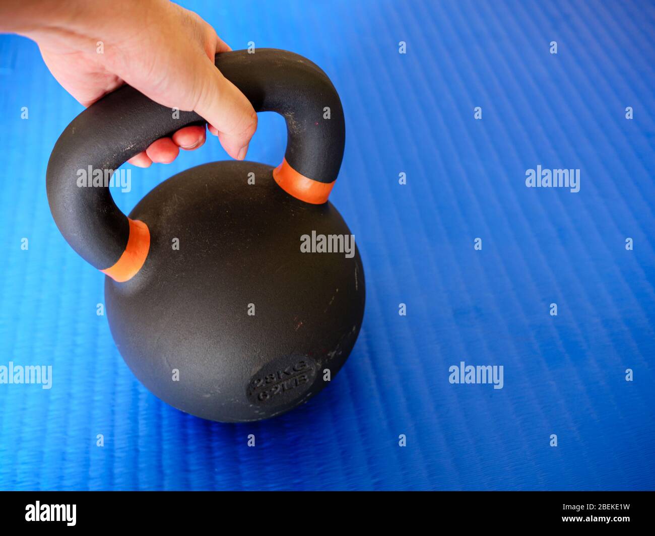 Hand hält schwarze Kettlebell auf blaue Fitness-Matte mit Copy Space - Home Workout Konzept Stockfoto