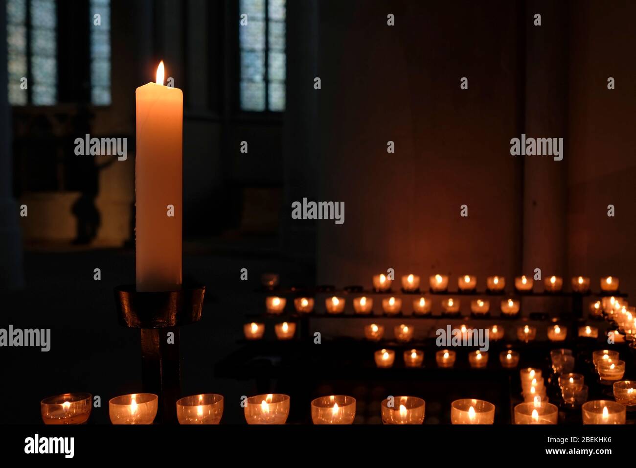 Eine große Kerze und viele kleine Kerzen beleuchten einen dunklen Kirchenraum Stockfoto