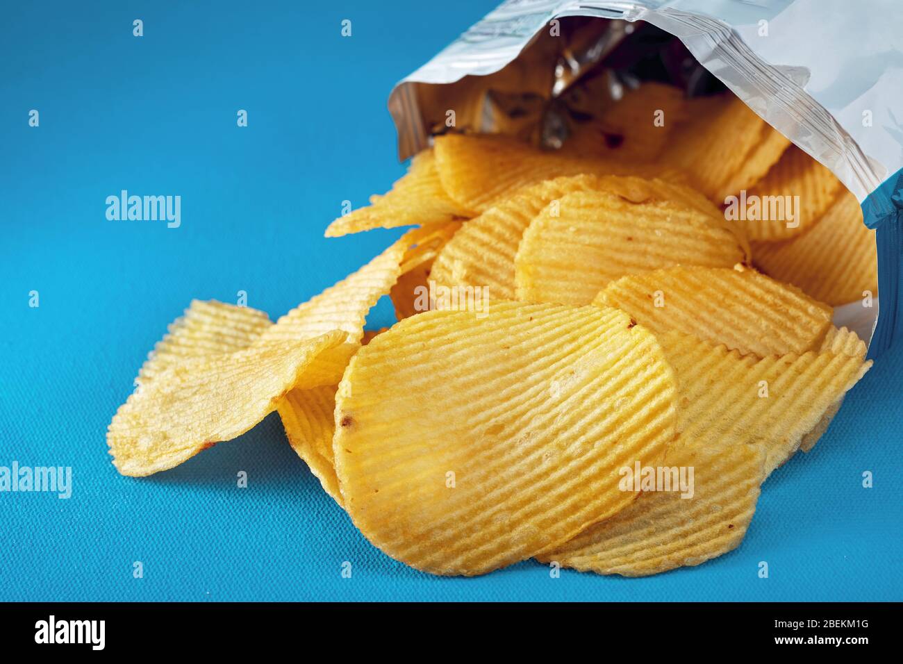 Kartoffelchips in einem Beutel oder einer Packung laufen auf dem Tisch aus. Makro Nahaufnahme. Stockfoto