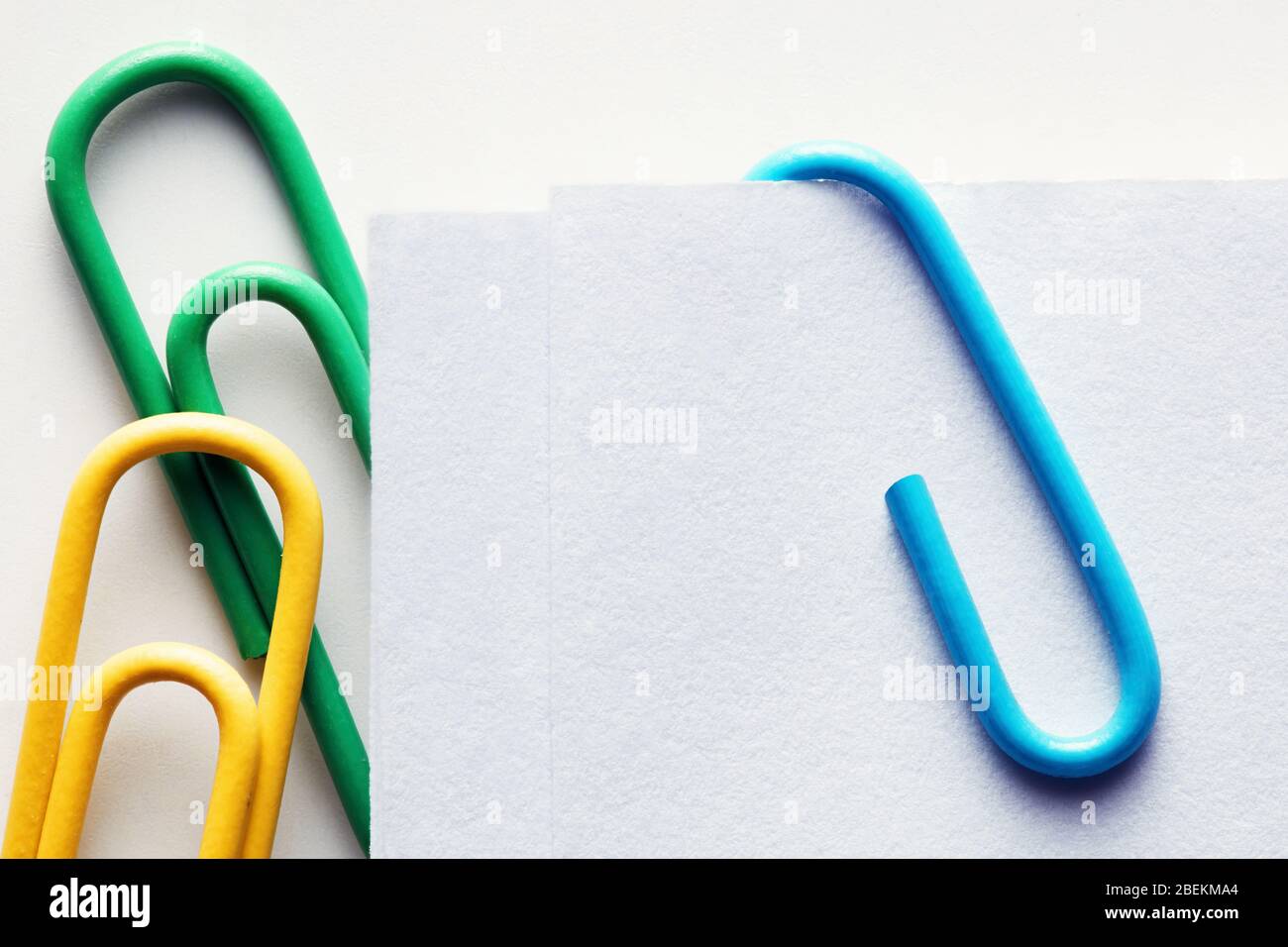 Bunte Büroklammern aus Kunststoff, die an einem weißen Papier befestigt sind. Nahaufnahme. Stockfoto